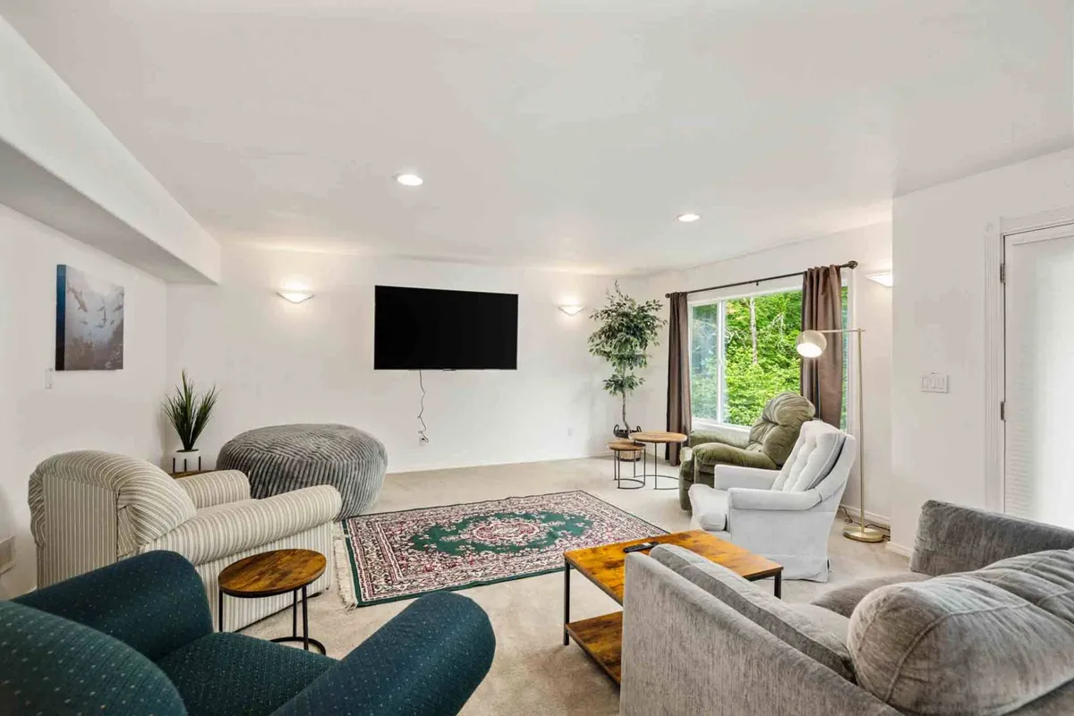 A bright, comfortable living area with a sofa, area rug, television, and a large window showcasing a view of greenery. The indoor plant and the abundance of natural light help blur the line between indoor and outdoor environments, making the space feel inviting for both work and relaxation.