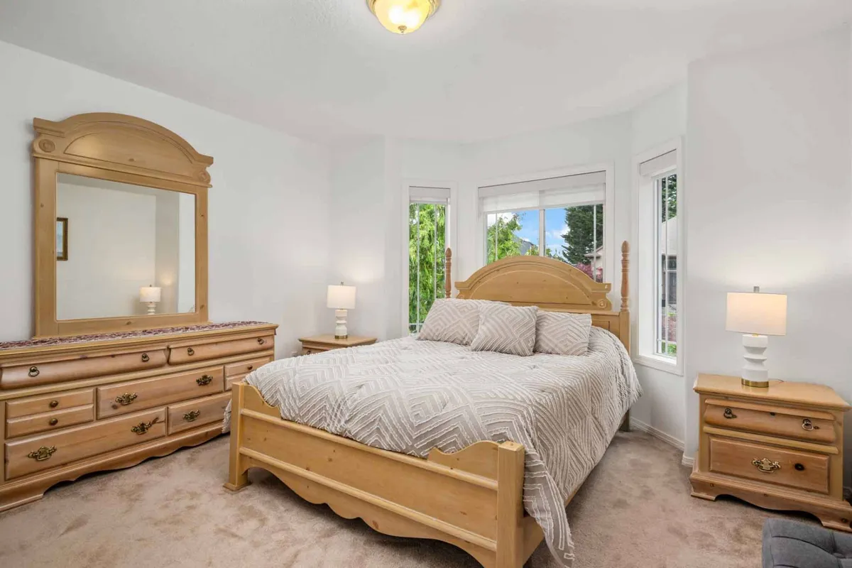 A tranquil bedroom with a comfortable bed, dresser, mirror, window letting in natural light, and a nightstand. The space feels serene and inviting, ideal for reading, relaxing, or sleeping.