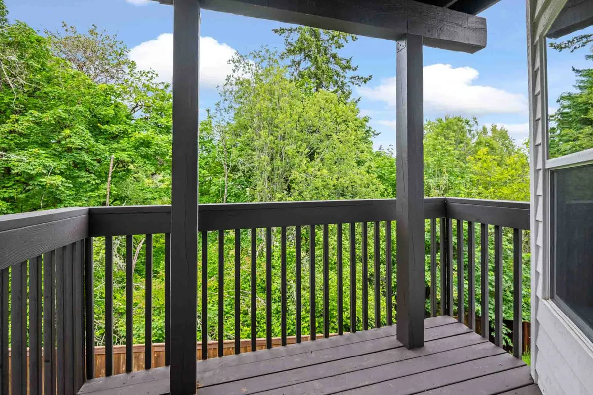 A serene deck with a wooden railing surrounded by lush greenery. The tranquil setting is perfect for enjoying fresh air, morning coffee, or simply relaxing above the woodland landscape.