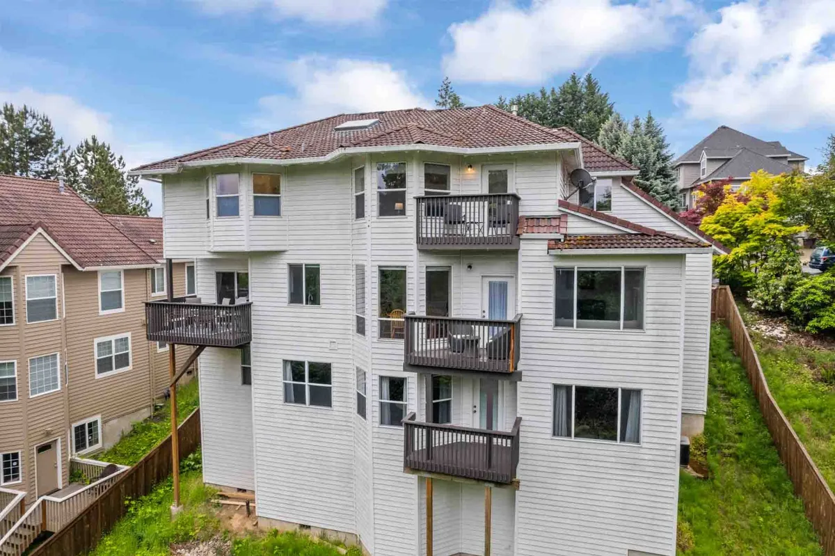 A view of the Manor's exterior, showcasing multiple balconies, large windows, and welcoming roof architecture. The scene is set for outdoor relaxation or gatherings, with hints of green landscaping surrounding the house.