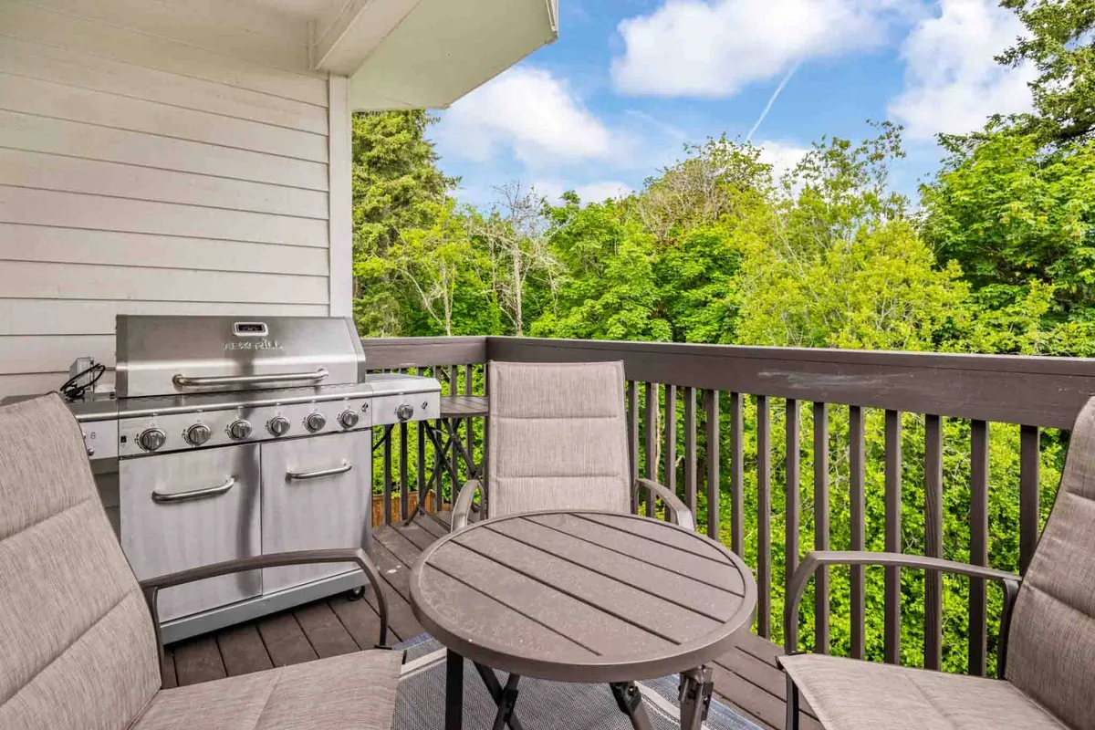 This exterior scene shows an outdoor grill area with seating, set against a backdrop of greenery. The space is casual and perfect for group gatherings or relaxing after a day out.