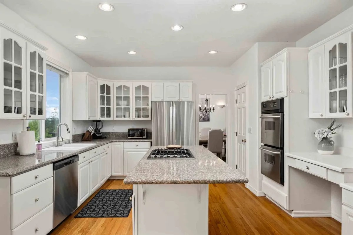 A welcoming, modern kitchen featuring a spacious central island with granite countertops, sleek appliances, and abundant natural light from generous windows. The layout invites group cooking and entertaining, with ample space for several people to prepare meals together.