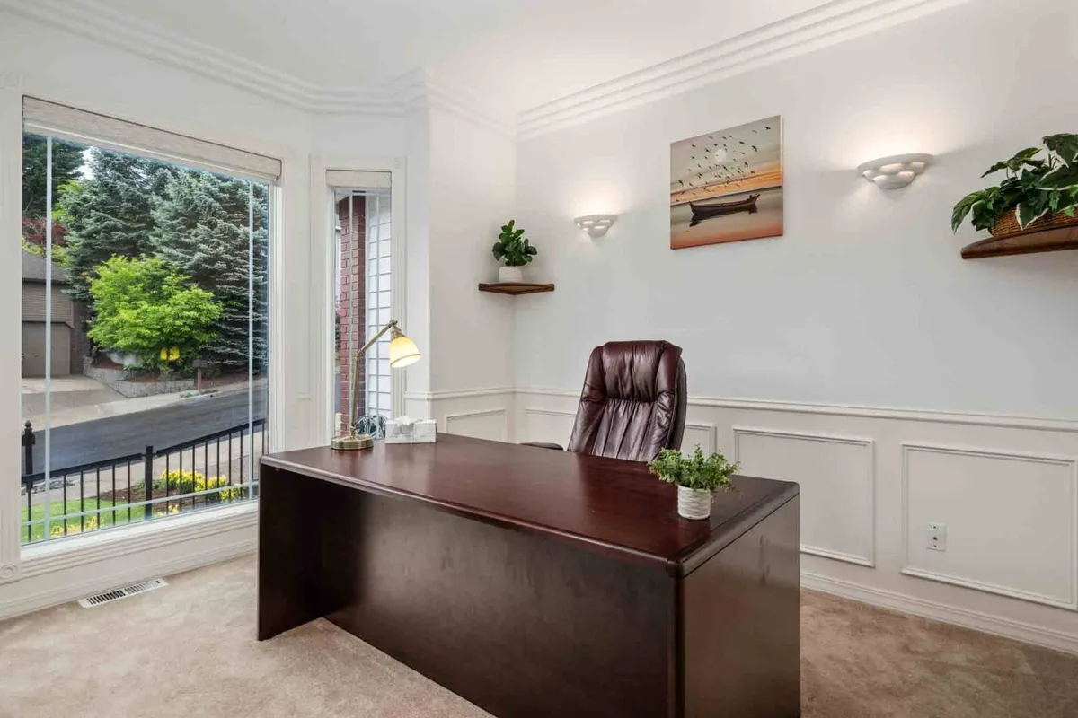 A focused and serene private office space with a wooden desk, leather chair, large window, green plants, and wall art. Ideal for working or reading in peace.
