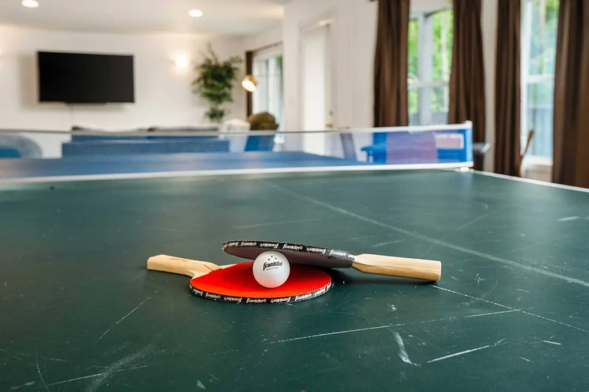 The image showcases a vibrant game room centered around a ping pong table, with paddles and a ball ready for play. The space is bright and inviting, perfect for friendly competitions or relaxing with family and friends.